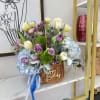 Basket arrangement of purple, white, and blue flowers with a birthday ribbon