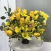 Yellow roses and daisies arranged in a black vase with green foliage.