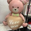 Pink teddy bear balloon holding a heart balloon that says 