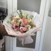 Hand-tied bouquet of pink and white mixed flowers wrapped in pale paper