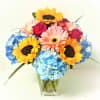 Bouquet of sunflowers, pink gerberas, roses, and blue hydrangeas in a clear vase