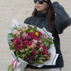 Woman holding a large bouquet of pink and magenta flowers wrapped in white paper