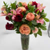 Bouquet of pink, peach, and red roses with lilies in a clear glass vase
