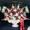 Red roses and white flowers arranged in a white vase with a red ribbon
