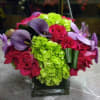 Bouquet of red roses, purple calla lilies, and green hydrangeas in a glass vase