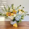 Bouquet of white roses, blue hydrangeas, and yellow orchids in a white vase