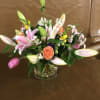 Mixed bouquet of pink lilies, orange roses, and assorted flowers in a glass vase