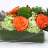 Orange roses and succulents arranged in a rectangular glass vase