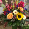 Colorful mixed bouquet in a tall green vase with roses and sunflowers