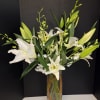 White lilies and orchid stems in a tall glass vase