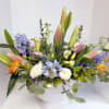 Mixed bouquet with lilies, blue flowers, and white blooms in a white vase