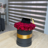 Red roses arranged in a black hat box with a graduation cap on top