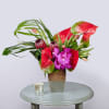 Tropical flower arrangement in a tall vase with red anthuriums and purple orchids