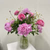 Pink peonies and roses with small white daisies arranged in a ribbed glass vase on a white pedestal