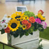 Mixed bouquet in a white wooden box with sunflowers, roses, and daisies