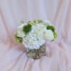 White floral bouquet in a clear glass vase with pale pink draping