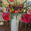 Large mixed flower arrangement in a white pedestal vase with pink and orange blooms