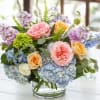 Pastel bouquet of roses, hydrangeas, and purple blooms in a glass vase