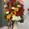 Mixed bouquet of red roses, yellow sunflowers, and white hydrangea in a decorative vase