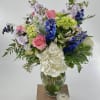 Mixed bouquet of pink roses, blue flowers, and white hydrangeas in a glass vase