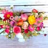 Colorful arrangement of roses, ranunculus, poppies, and snapdragons in a white pedestal vase