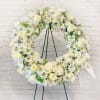 White floral wreath on a stand with roses and daisies