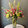Tall mixed arrangement of pink and yellow tulips, green hydrangeas, and Bells of Ireland in a clear glass vase