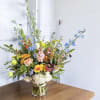 Tall mixed bouquet in a clear glass vase with blue and peach flowers