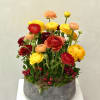 Low gray bowl filled with tall yellow, orange, and red blooms accented with red berries.
