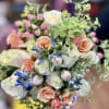 Bouquet of white, blush, and peach roses with blue flowers and pink berries