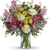 Mixed bouquet of pink, yellow, purple, and white flowers in a glass vase