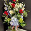 Bouquet of red and white roses with blue flowers in a glass vase
