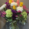 Mixed bouquet of yellow roses, white mums, and pink and green blooms in a clear glass vase