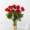 Tall arrangement of red roses in a clear glass vase with a gold base