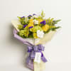 Yellow roses and white flowers in a wrapped bouquet with a purple ribbon