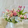 Pink roses and tulips arranged with blue hydrangeas in a white vase.