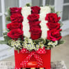 Red and white roses arranged in a red gift box with chocolates and a polka-dot ribbon