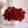 Low white vase filled with many red roses on a round marble table