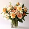 Peach and yellow rose arrangement with white accents in a clear glass vase.
