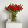 A dense cluster of red tulips gathered into a clear glass vase