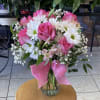 Pink roses and white daisies arranged in a glass vase with a pink ribbon