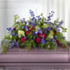 Large floral casket spray with blue, purple, pink, and white flowers