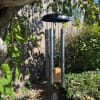 Black memorial wind chime hanging outdoors among trees and shrubs