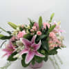 Large pink lilies burst open above a cloud of soft pink roses