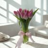 Pink tulips in a clear glass vase with a pink ribbon