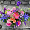 Vibrant mixed arrangement of pink peonies, roses, and purple irises in a clear glass vase