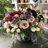 Mixed bouquet with pale roses, dark orchids, and succulents in a stone vase