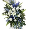 Tall standing spray of white lilies and roses with blue delphinium accents