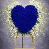 A striking heart-shaped standing tribute designed with deep blue roses and accented