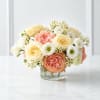 Low round arrangement of peach, cream, and white flowers in a clear glass vase